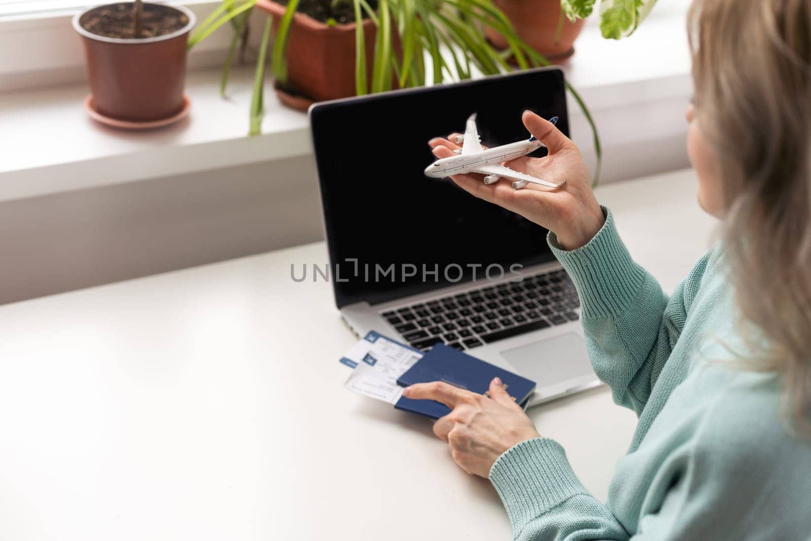 Positive happy woman going on summer holidays, sitting at office with toy plane and showing passport, having video call.