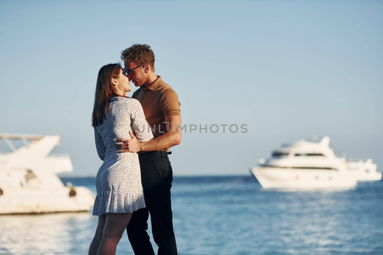 Sea and yacht at background. Happy young couple is together on their vacation. Outdoors at sunny daytime.