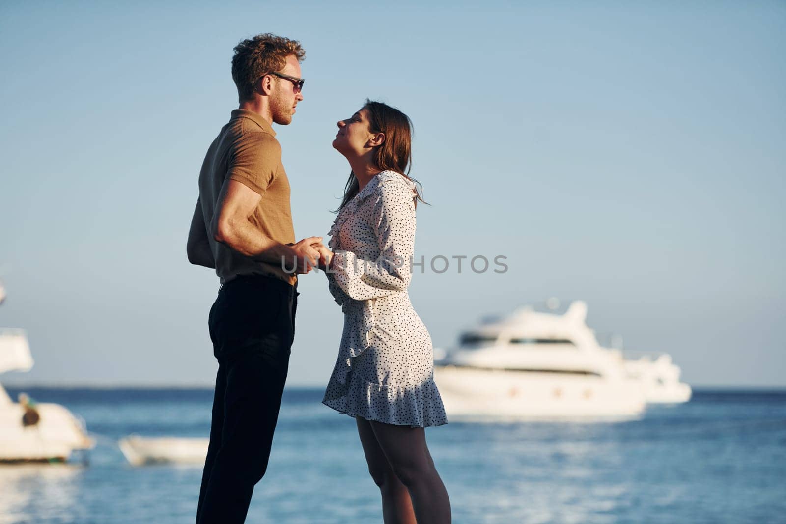 Sea and yacht at background. Happy young couple is together on their vacation. Outdoors at sunny daytime.