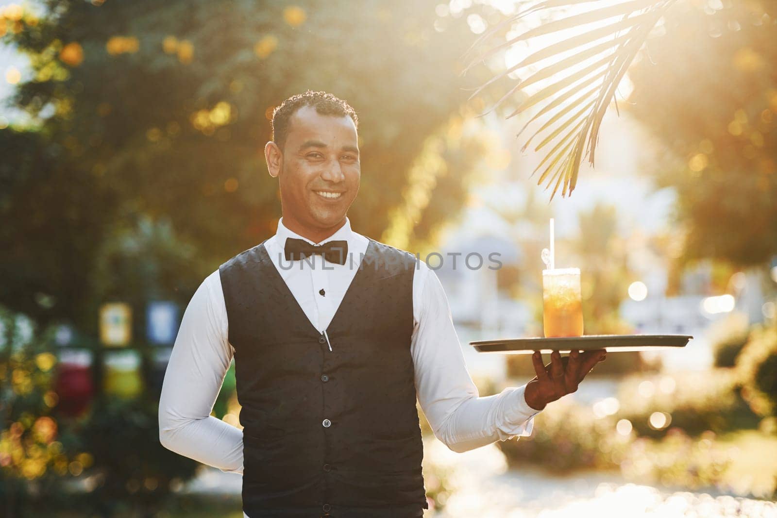 With order in hand. Black waiter in formal clothes is at his work outdoors at sunny daytime.