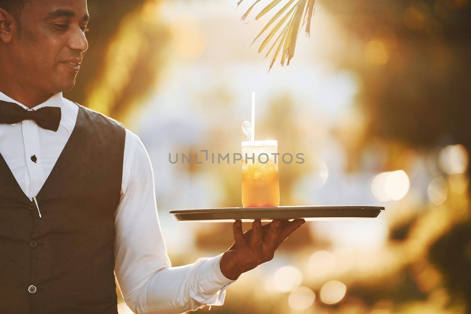 With order in hand. Black waiter in formal clothes is at his work outdoors at sunny daytime.