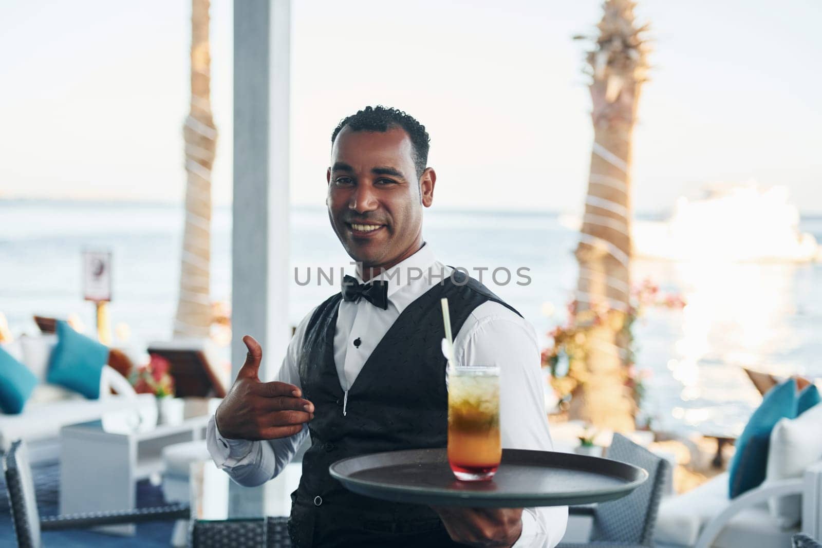 With order in hand. Black waiter in formal clothes is at his work outdoors at sunny daytime.