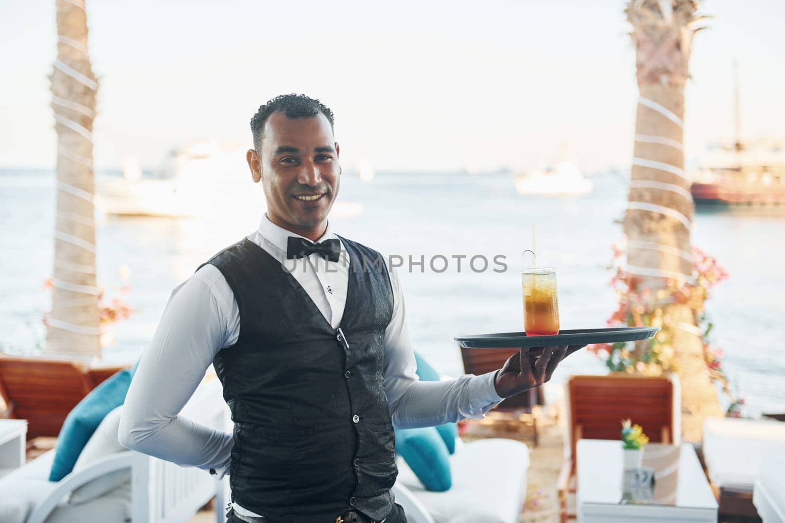 With order in hand. Black waiter in formal clothes is at his work outdoors at sunny daytime.