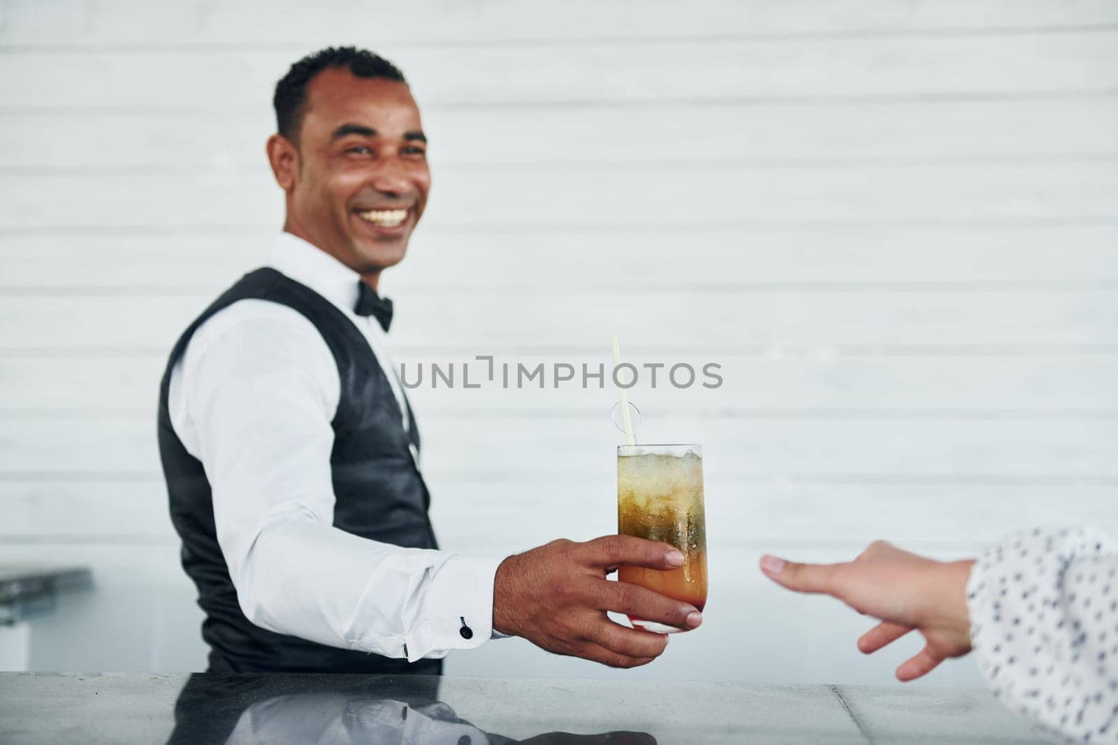 With order in hand. Black waiter in formal clothes is at his work outdoors at sunny daytime.