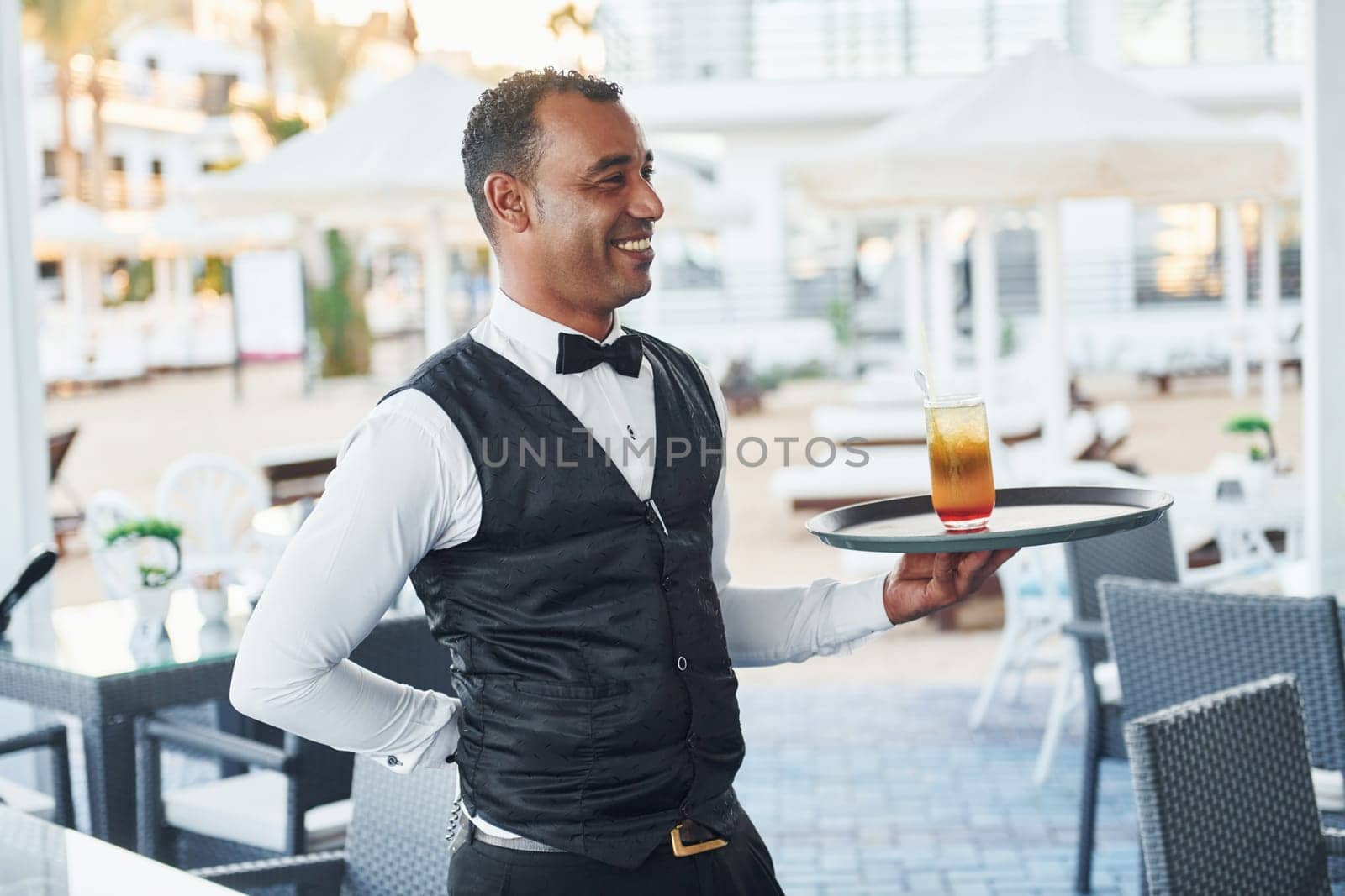 Black waiter in formal clothes is at his work outdoors at sunny daytime.