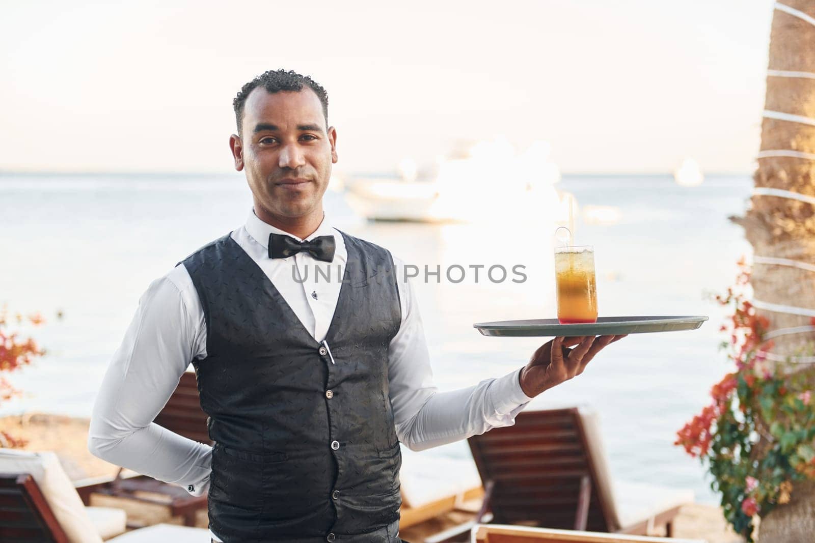 Black waiter in formal clothes is at his work outdoors at sunny daytime.