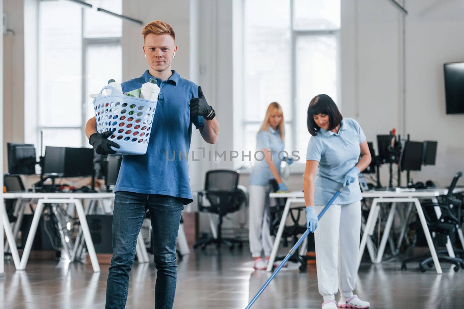 Man holds basket. Group of workers clean modern office together at daytime.