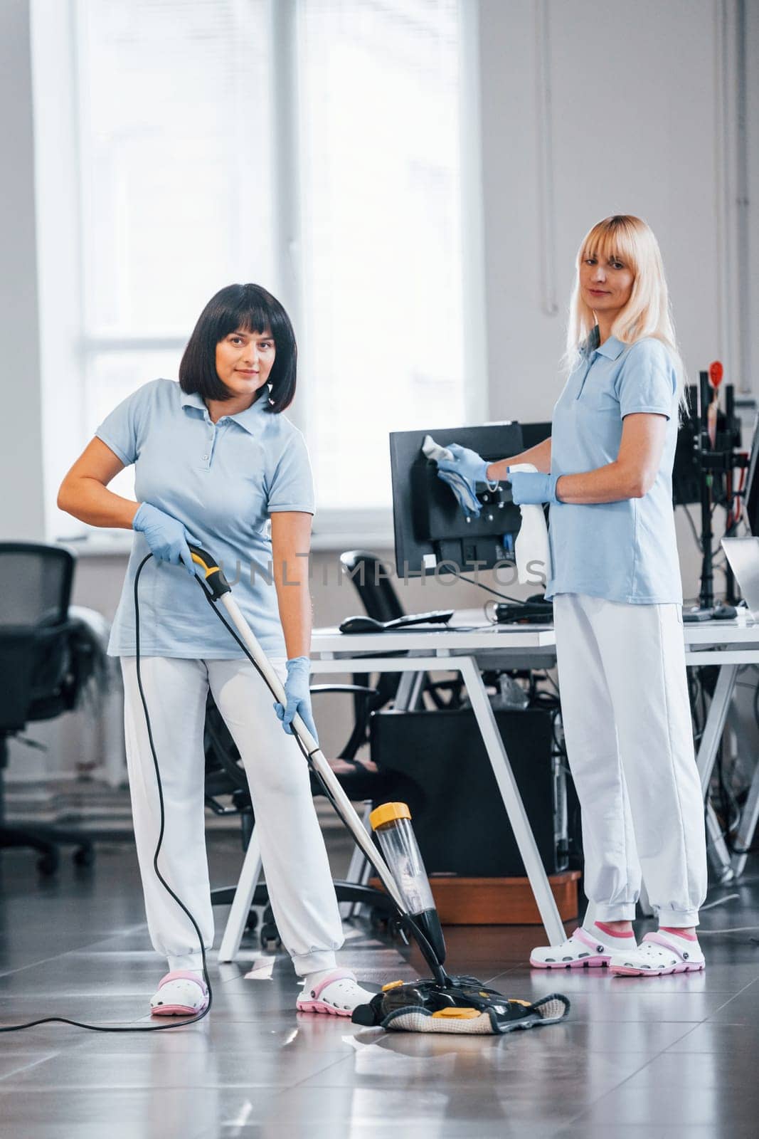Woman uses vacuum cleaner. Group of workers clean modern office together at daytime by Standret
