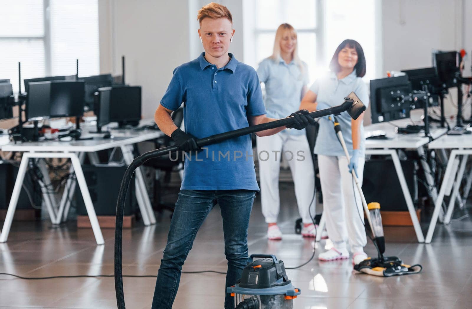 Guy with vacuum cleaner. Group of workers clean modern office together at daytime.