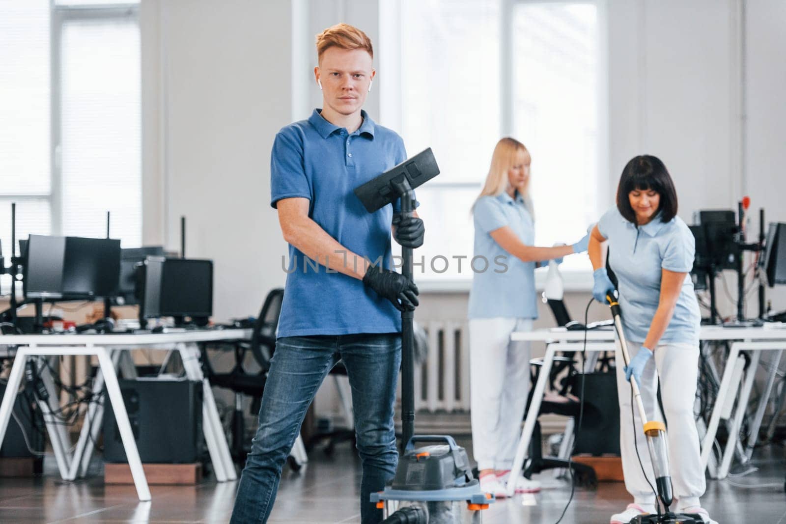 Guy with vacuum cleaner. Group of workers clean modern office together at daytime.