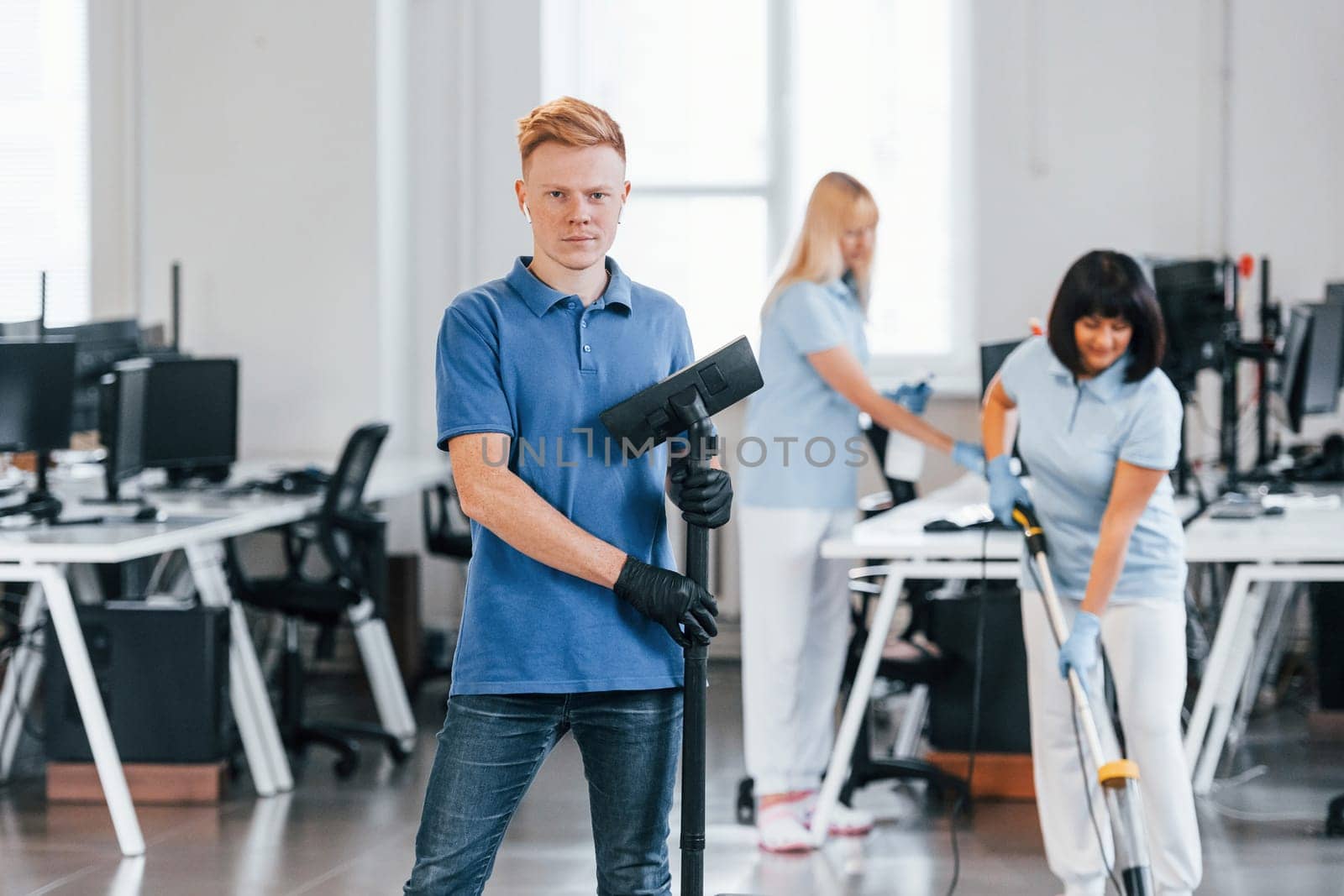 Guy with vacuum cleaner. Group of workers clean modern office together at daytime.