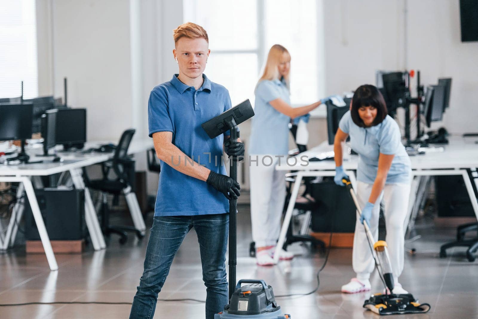 Guy with vacuum cleaner. Group of workers clean modern office together at daytime.