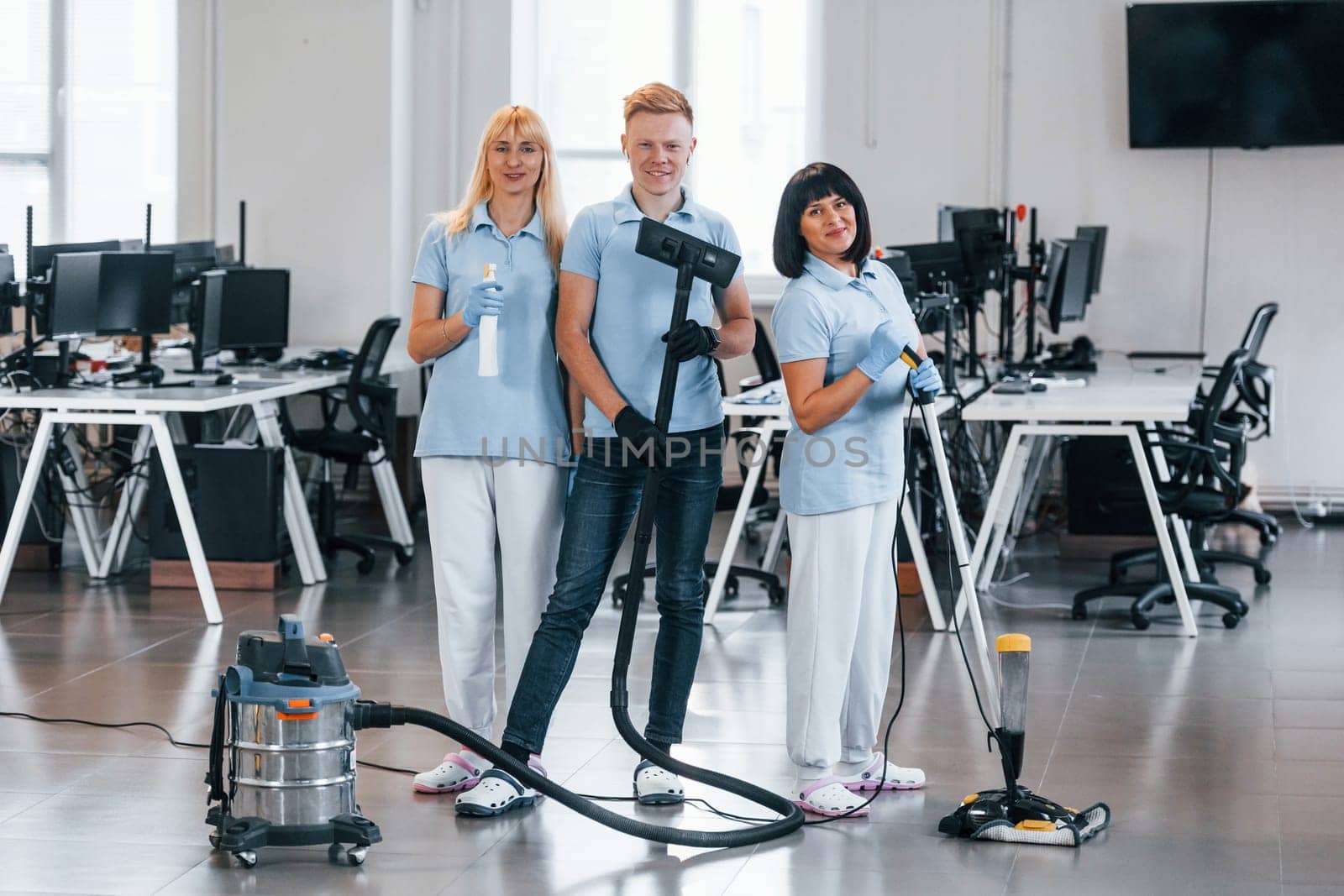 Guy with vacuum cleaner. Group of workers clean modern office together at daytime.