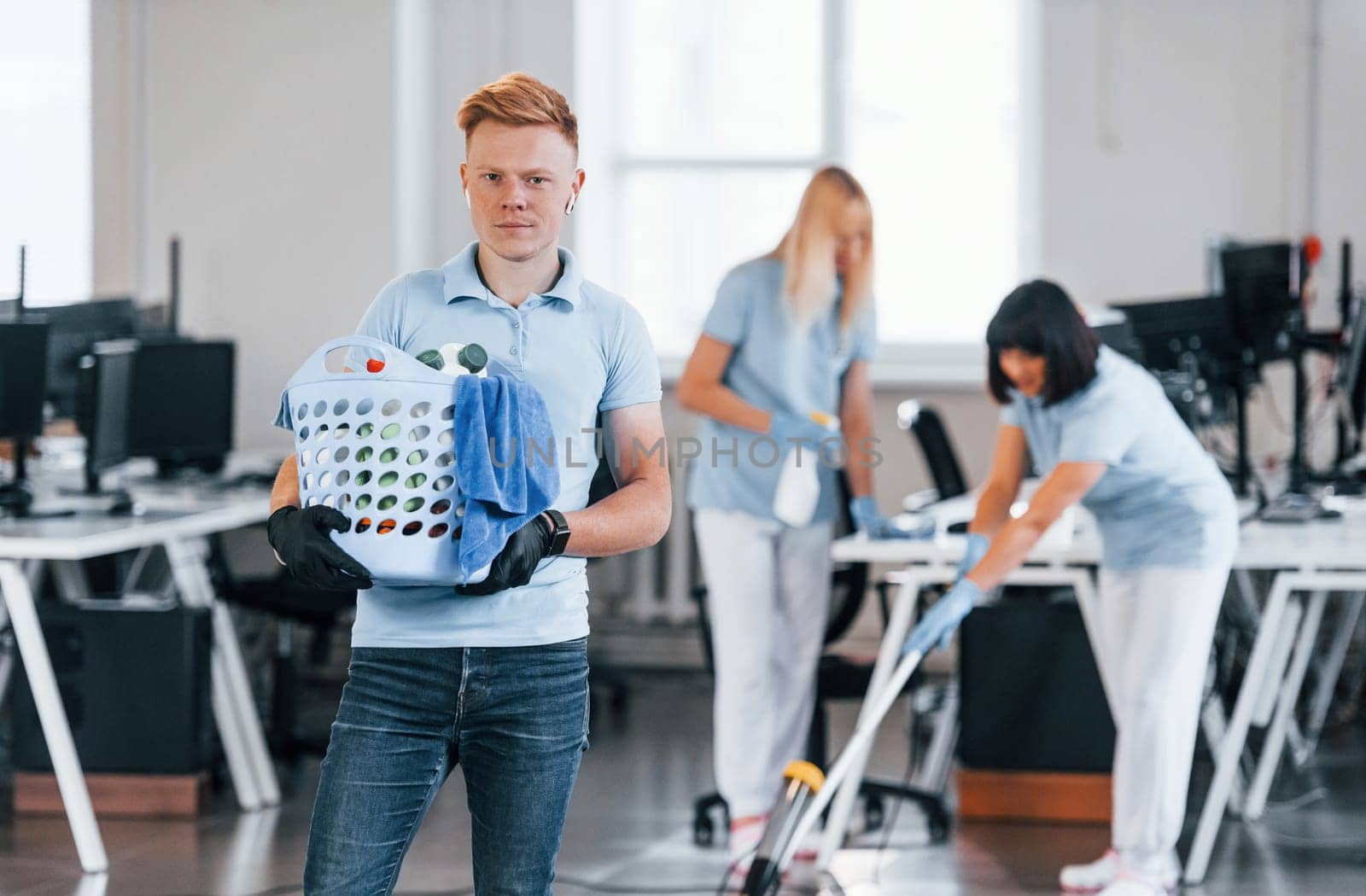 Man holds basket. Group of workers clean modern office together at daytime.