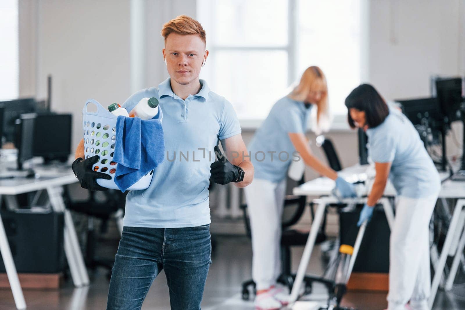Man holds basket. Group of workers clean modern office together at daytime.