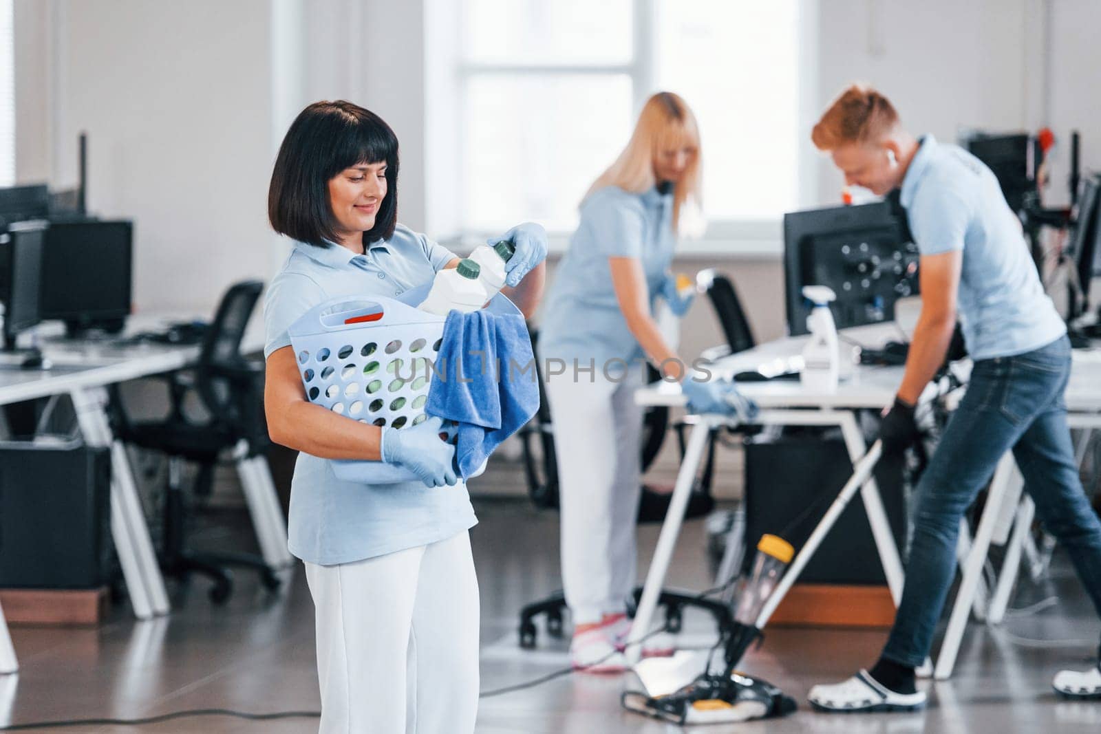 Woman with basket. Group of workers clean modern office together at daytime.