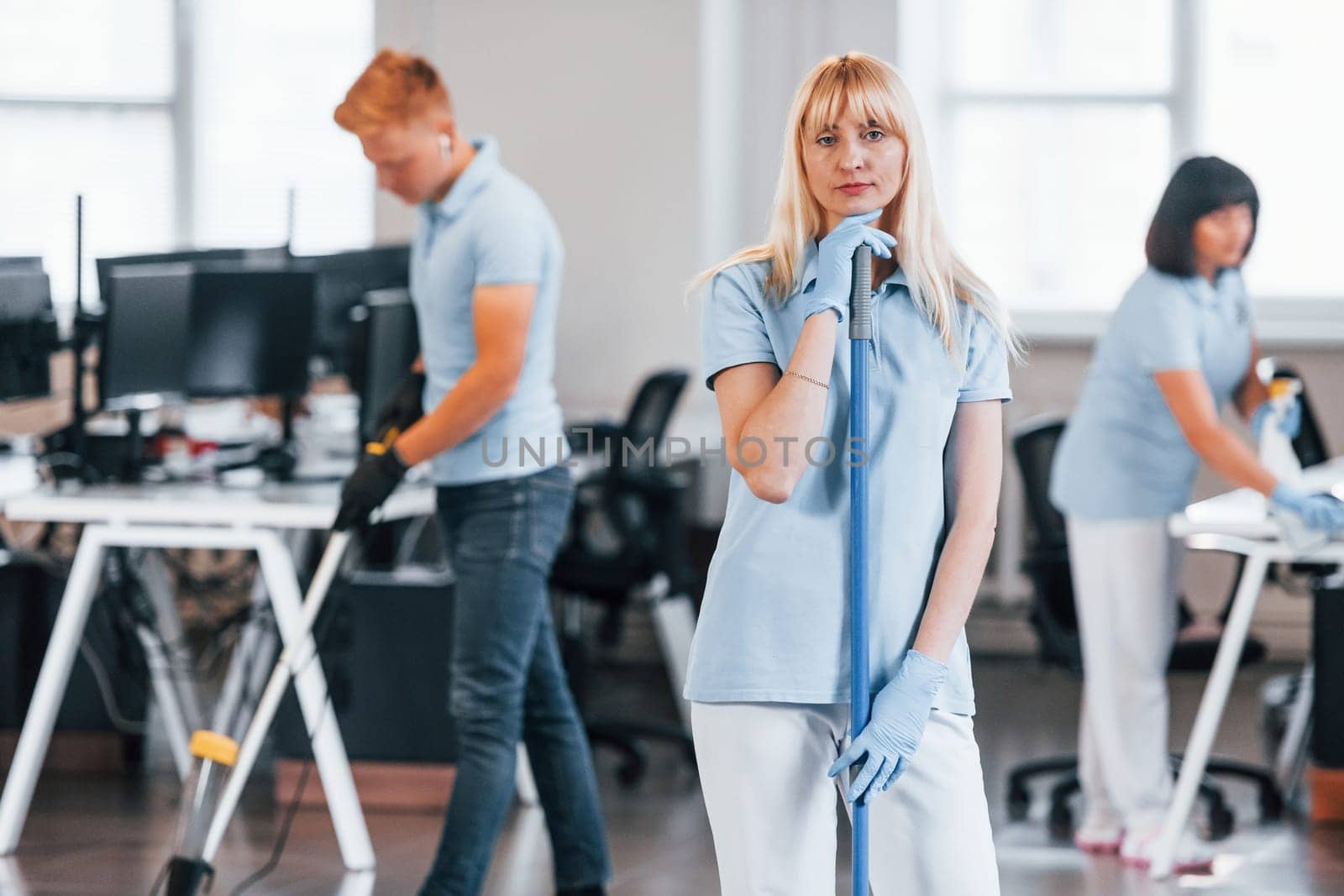 Cleans floor. Group of workers clean modern office together at daytime.
