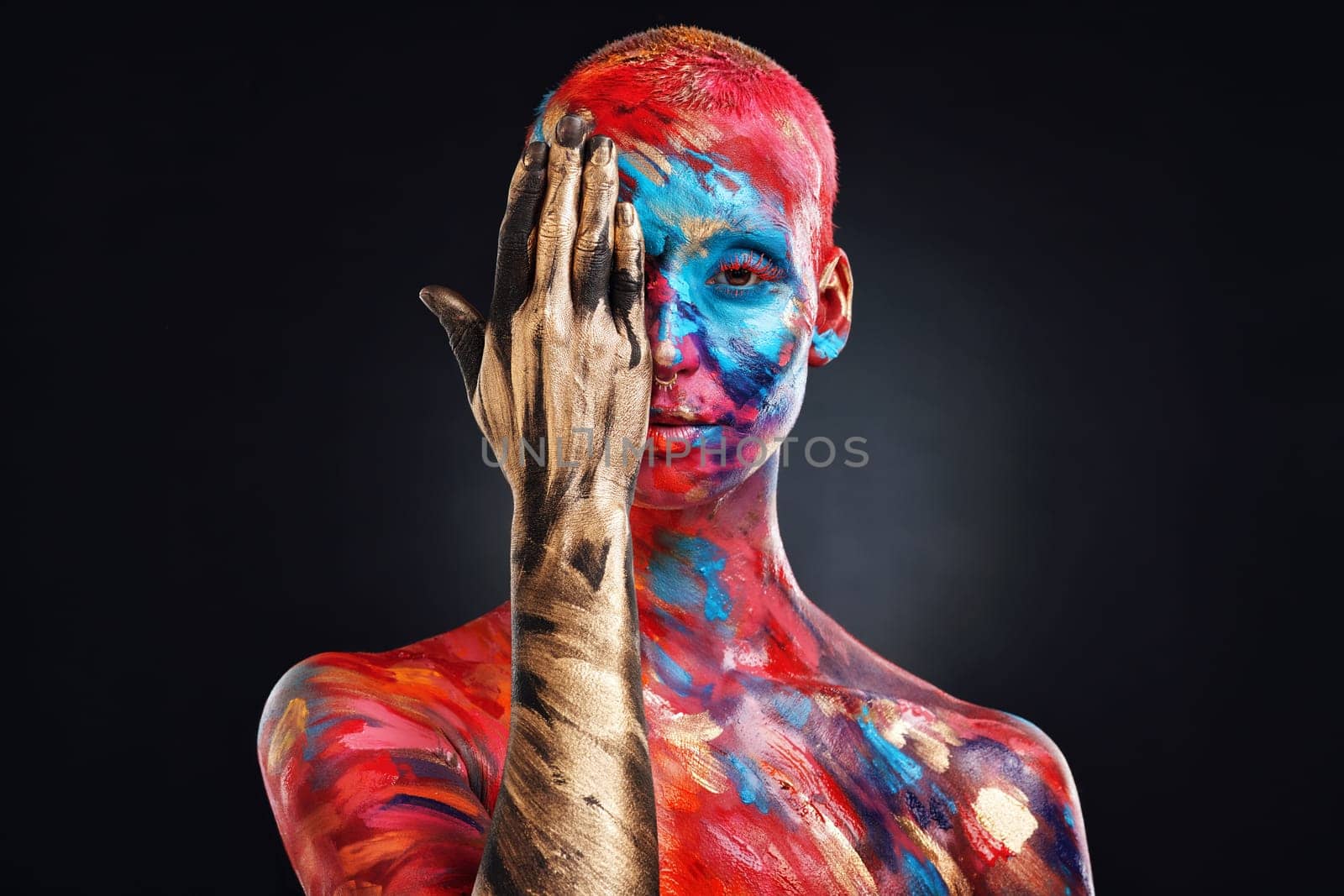 Paint the world how you see fit. an attractive young woman posing alone in the studio with paint on her face. by YuriArcurs