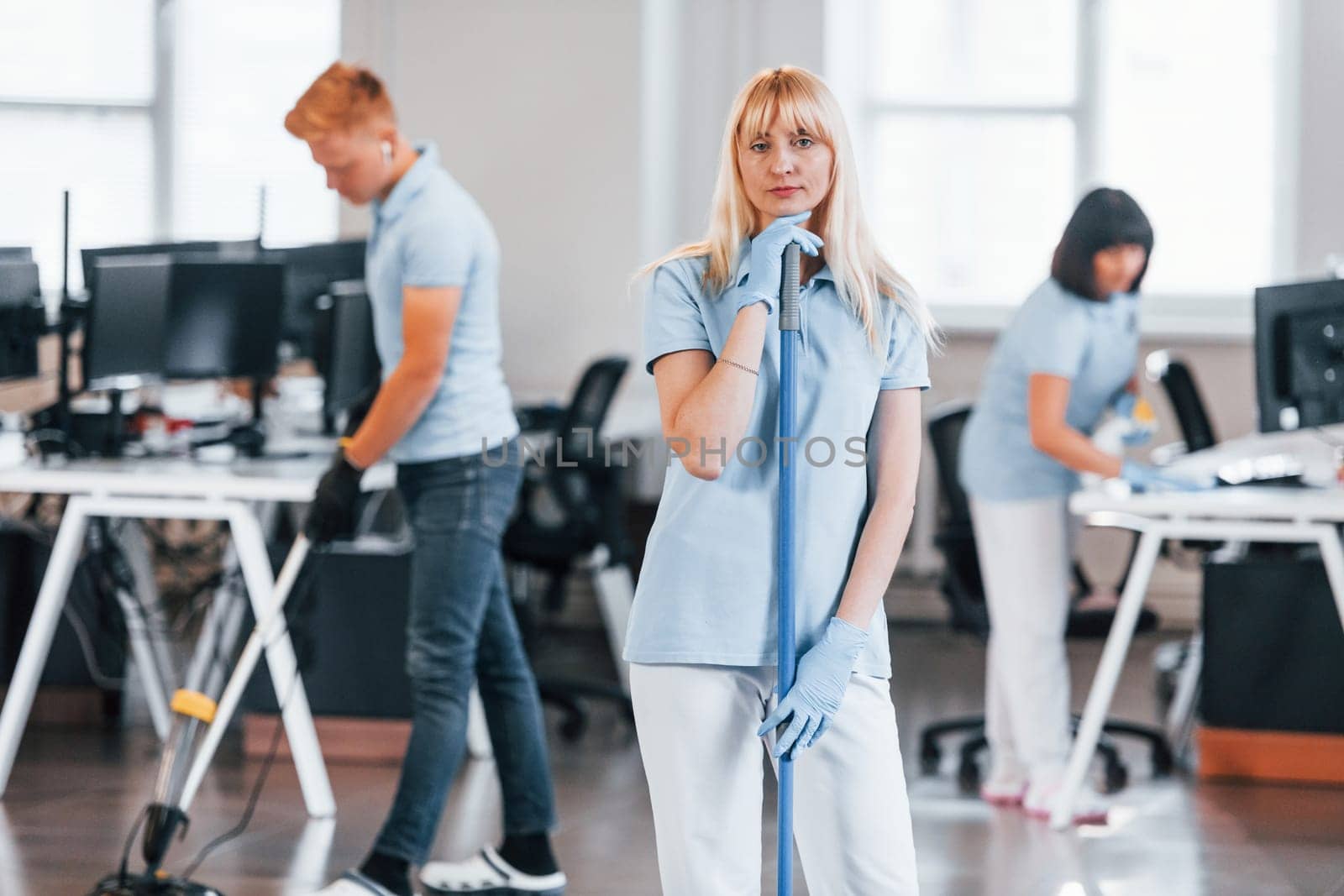 Cleans floor. Group of workers clean modern office together at daytime.