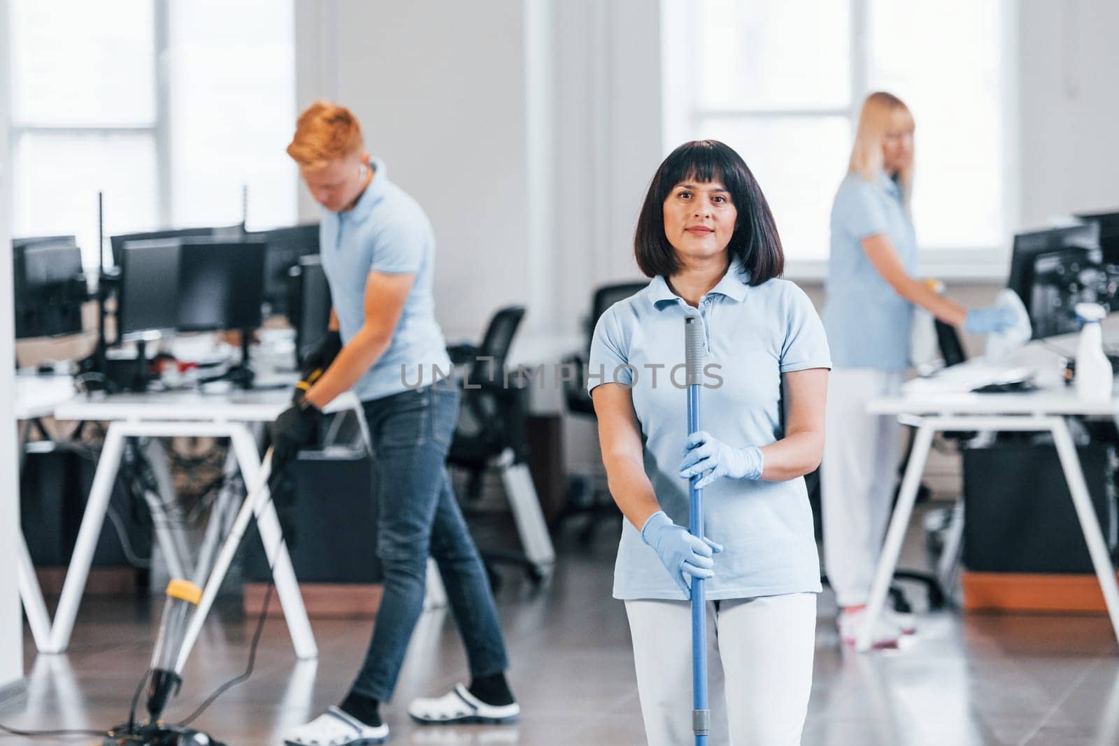 Cleans floor. Group of workers clean modern office together at daytime.