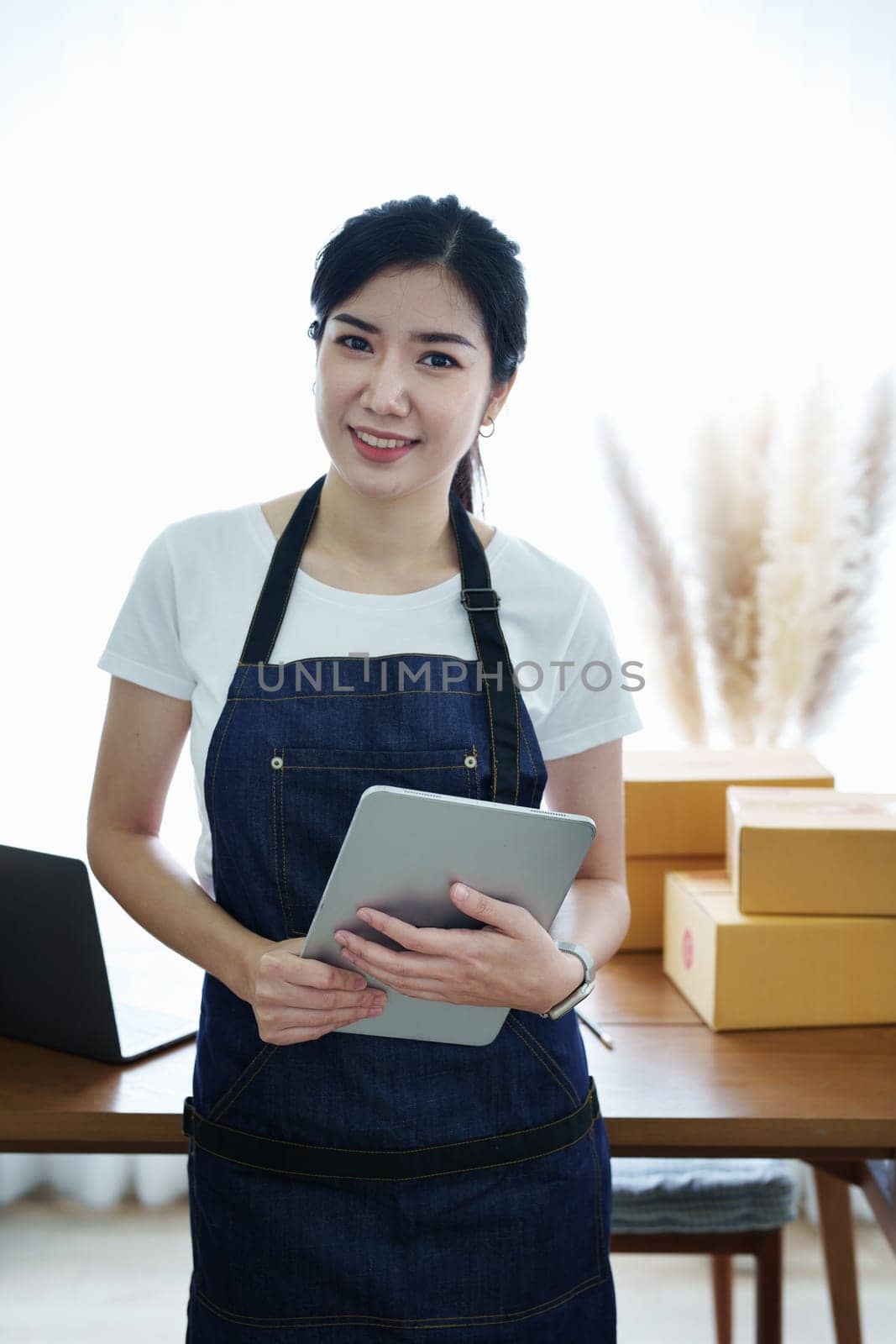 Starting small business entrepreneur of independent Asian woman smiling using tablet computer with cheerful success of online marketing package box items and SME delivery concept.