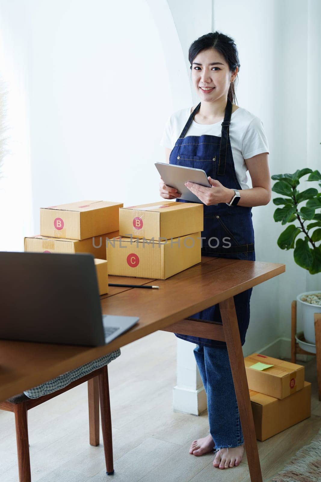 Starting small business entrepreneur of independent Asian woman smiling using tablet computer with cheerful success of online marketing package box items and SME delivery concept.