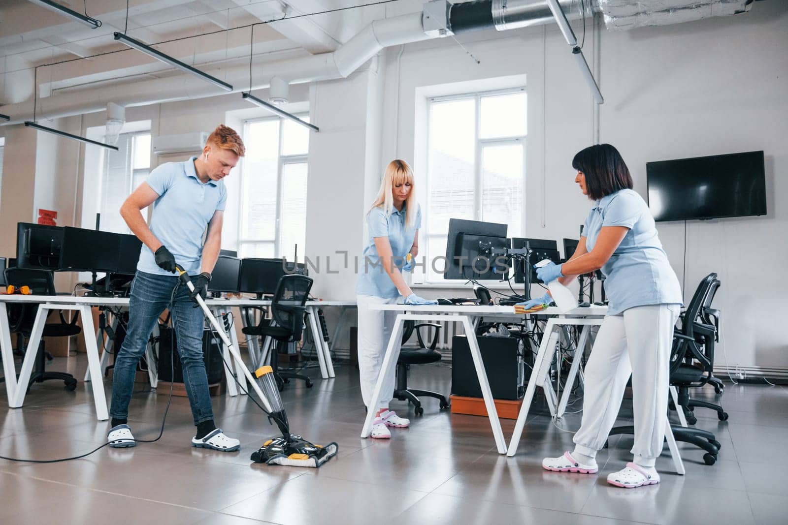 Cleans floor. Group of workers clean modern office together at daytime.