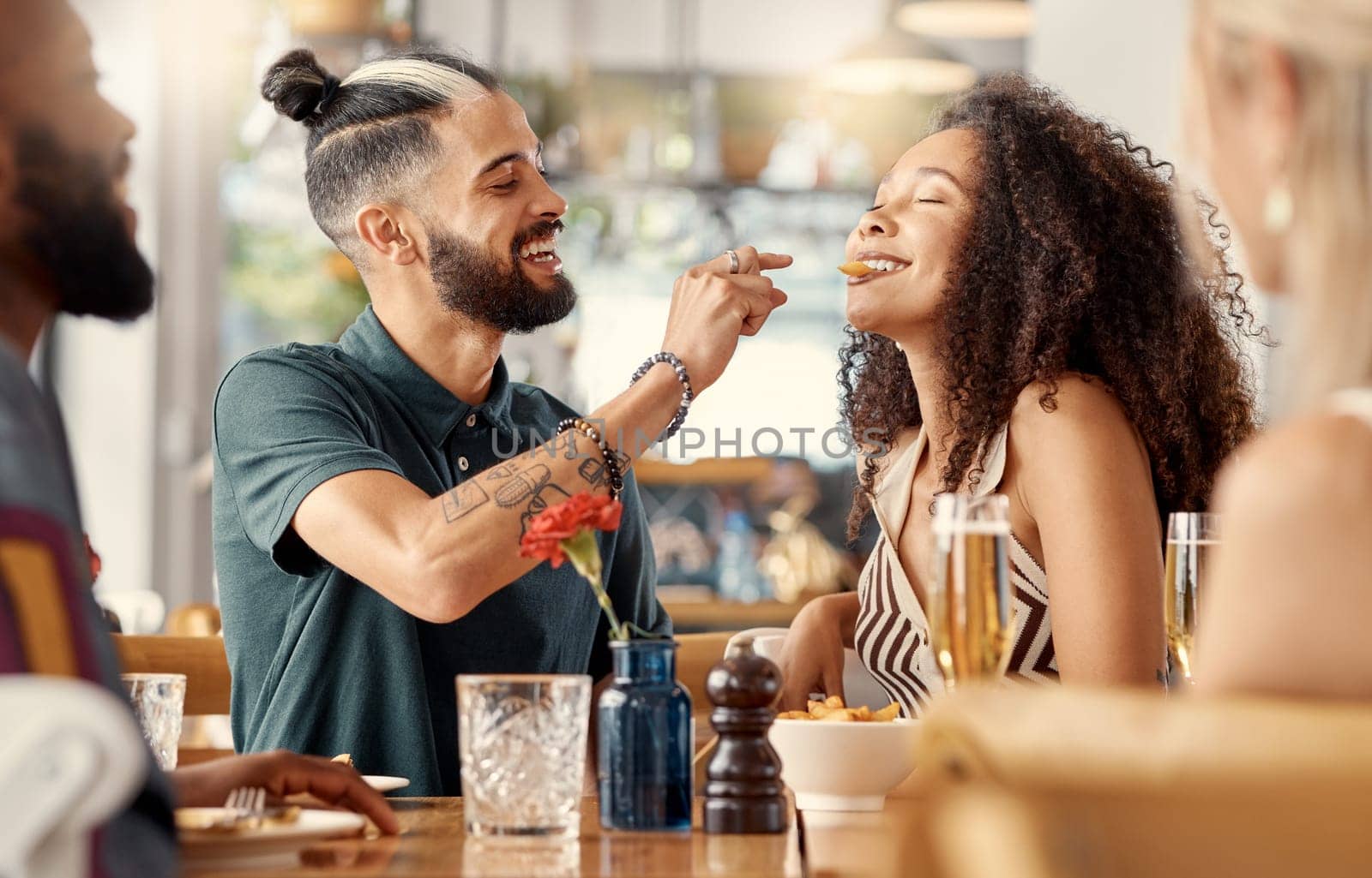A taste of the good life. a young man feeding his girlfriend fries in a restuarant