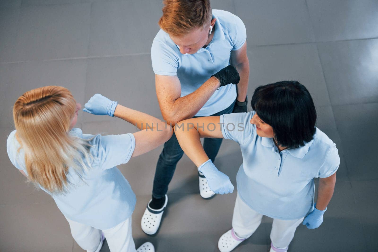 Touches by the elbows. Group of workers clean modern office together at daytime.