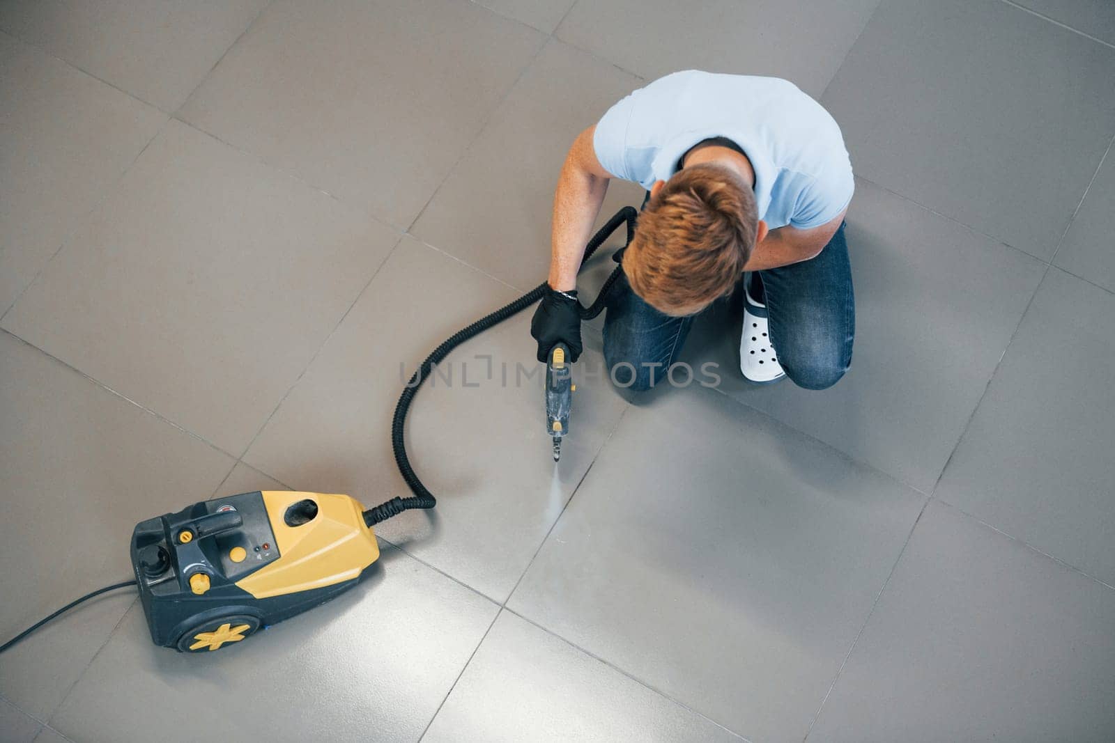 Top view of man in blue shirt and protective gloves that uses vacuum cleaner.