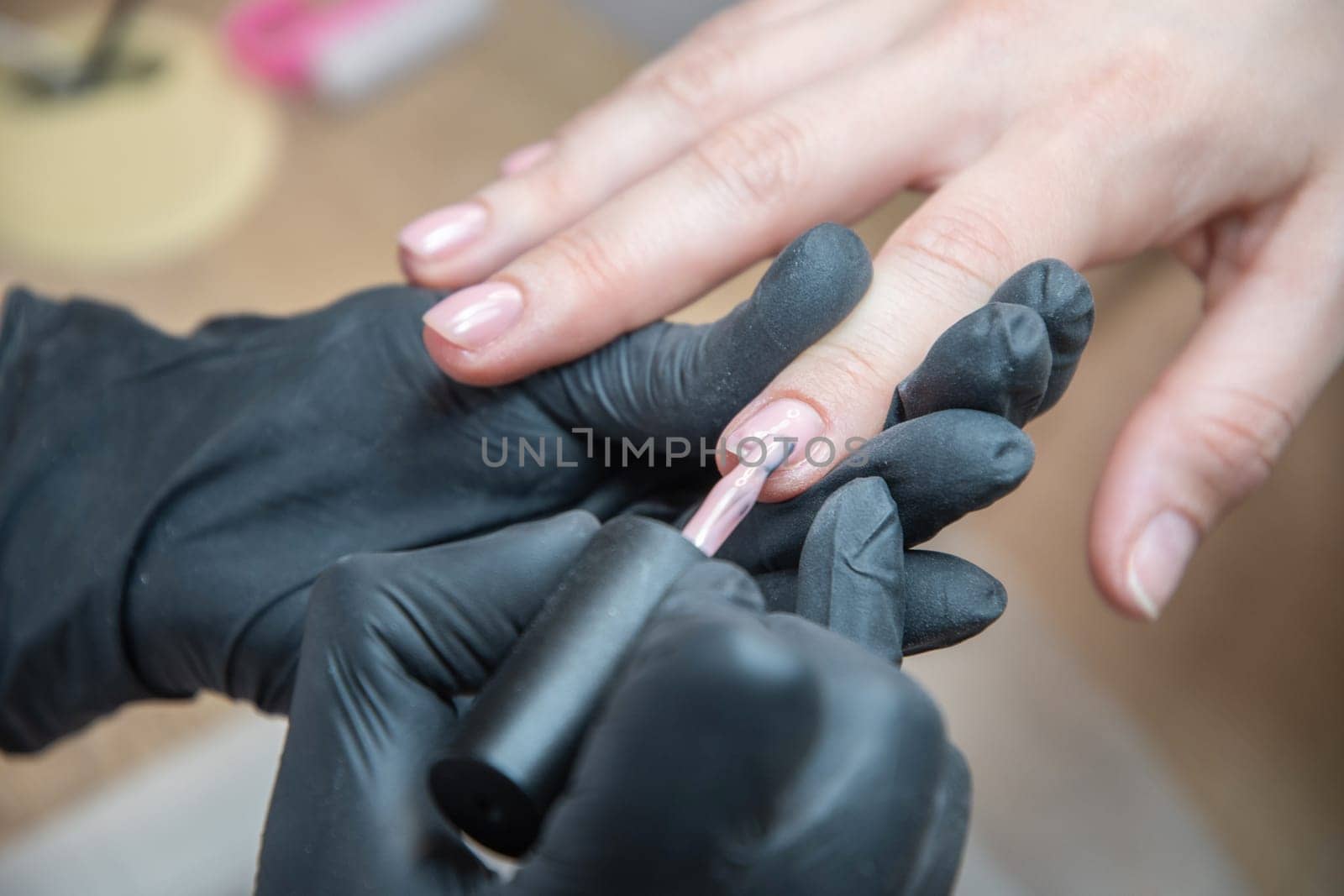 a master does a manicure to a client in a beauty salon and covers her nails with pink varnish. High quality photo