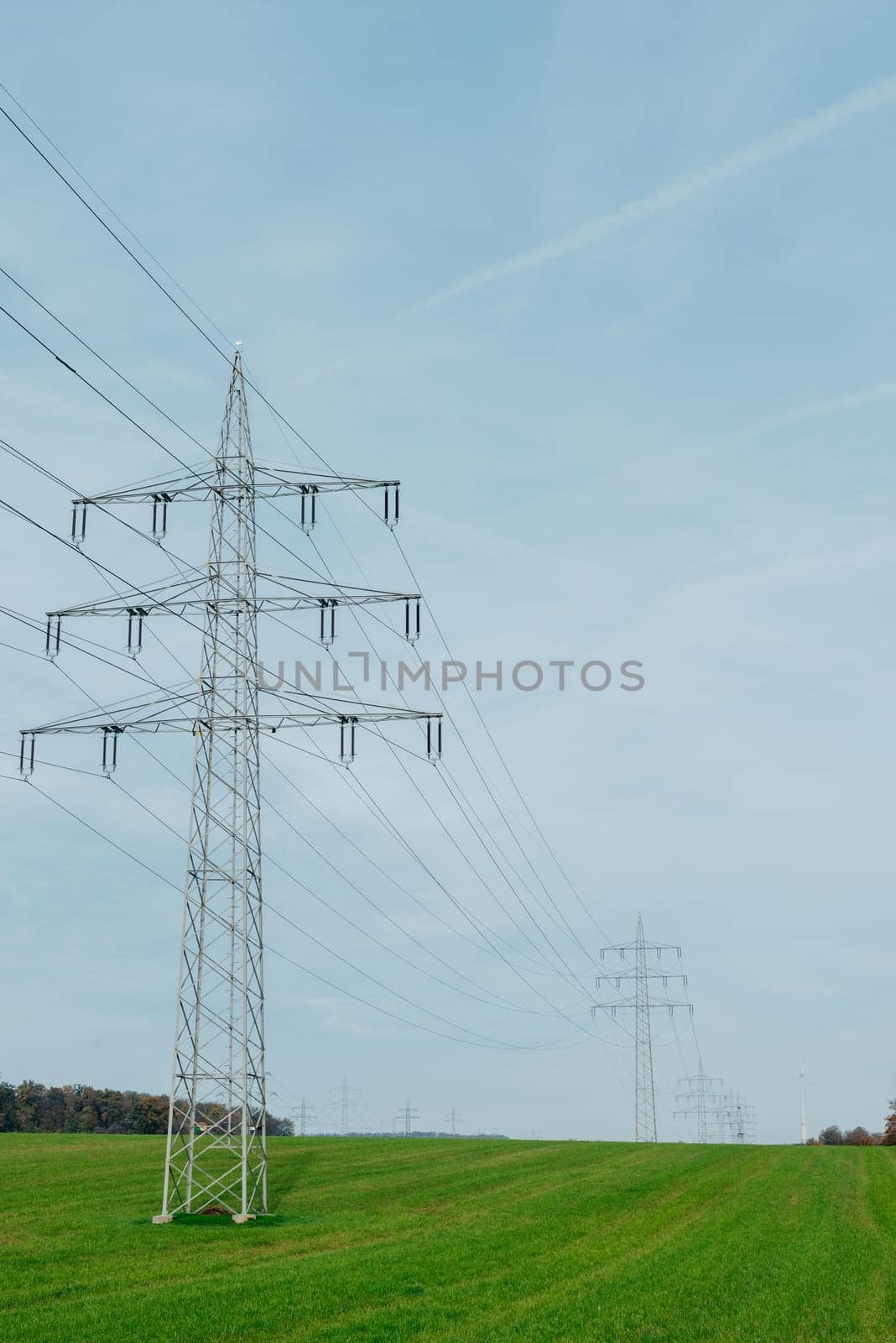 High voltage power lines leading through a green field. Transmission of electricity by means of supports through agricultural areas.