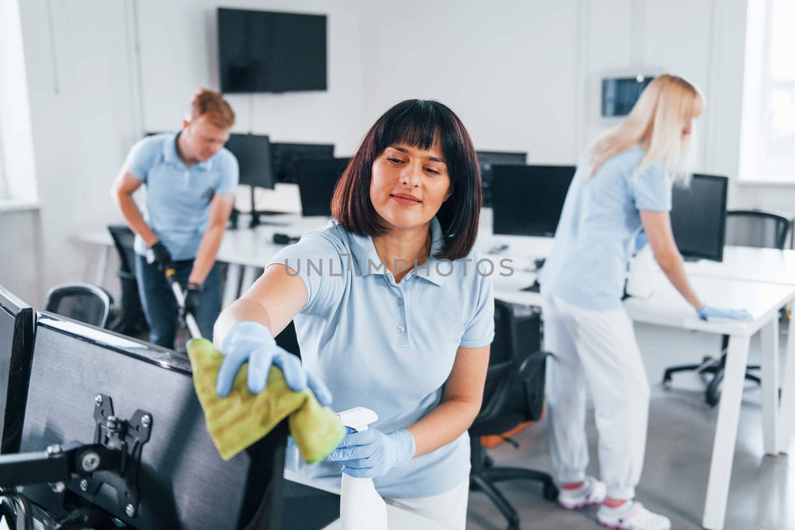 Cleans monitor. Group of workers clean modern office together at daytime.