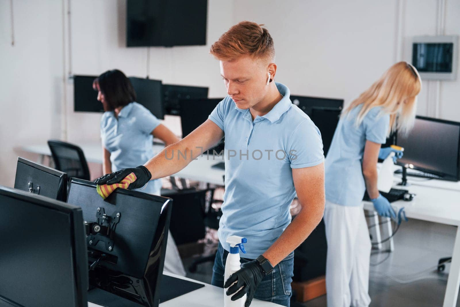 Cleans monitor. Group of workers clean modern office together at daytime.