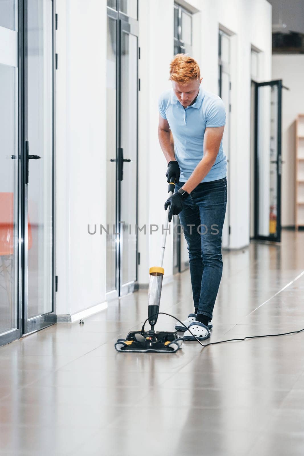 Young man works in the modern office. Uses vacuum cleaner.