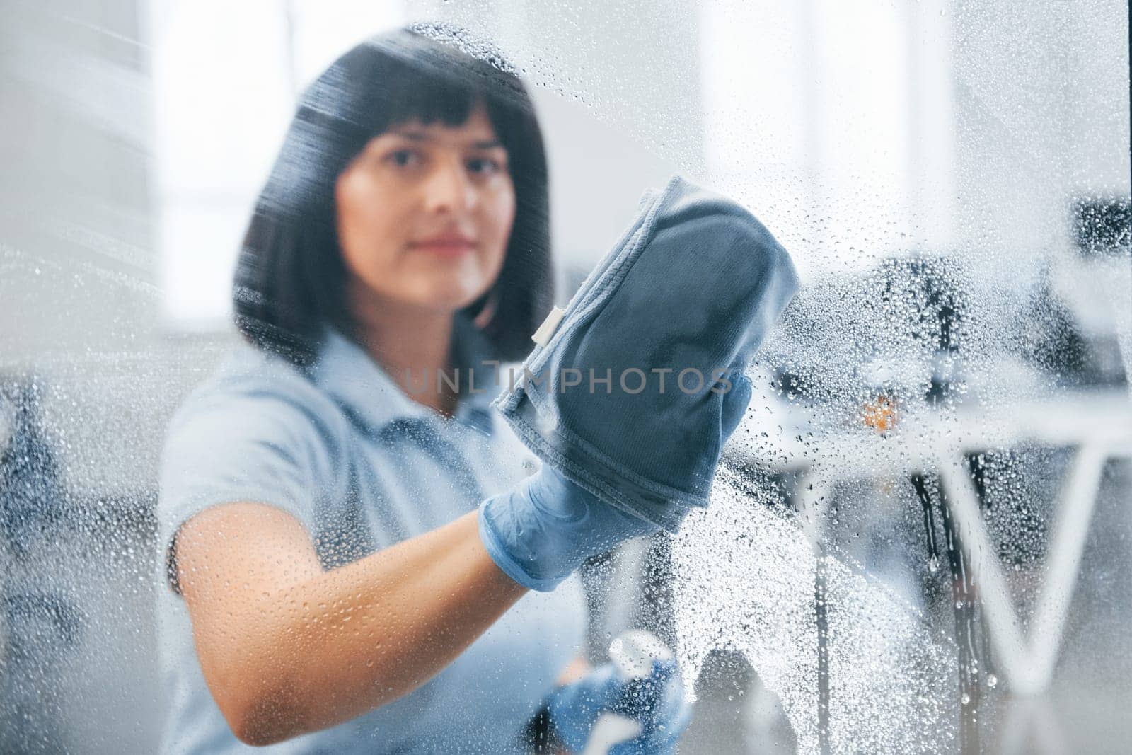 Woman cleaning dirty window by using towel. View through the glass.