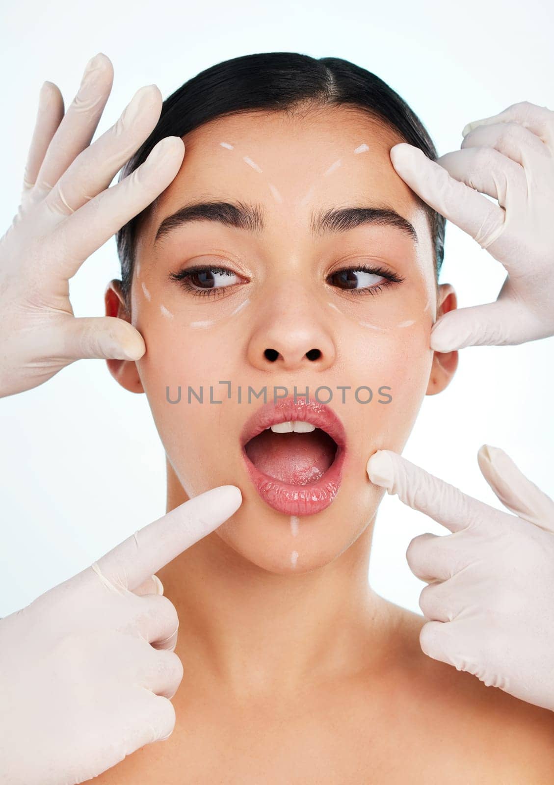 Many hands make light work. Studio shot of an attractive young woman having some plastic surgery done against a light background. by YuriArcurs