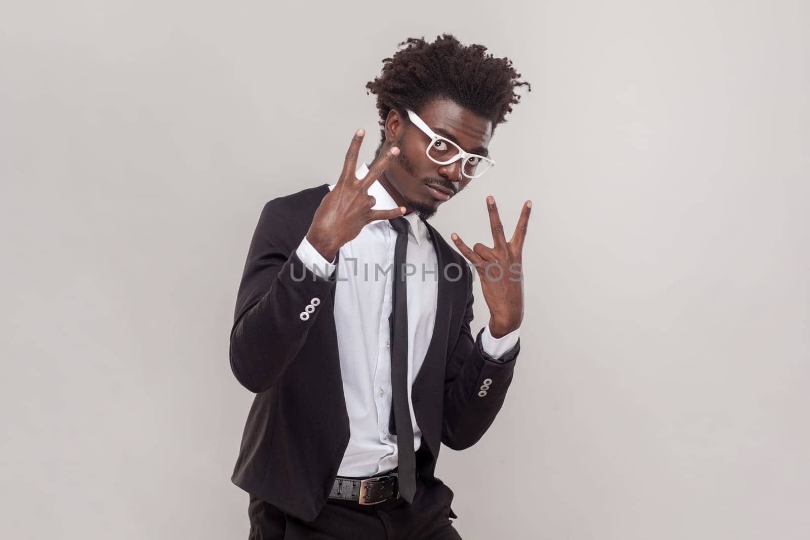 Portrait of aggressive man in glasses standing looking at camera, showing shocker gesture, wearing white shirt and tuxedo. Indoor studio shot isolated on gray background.