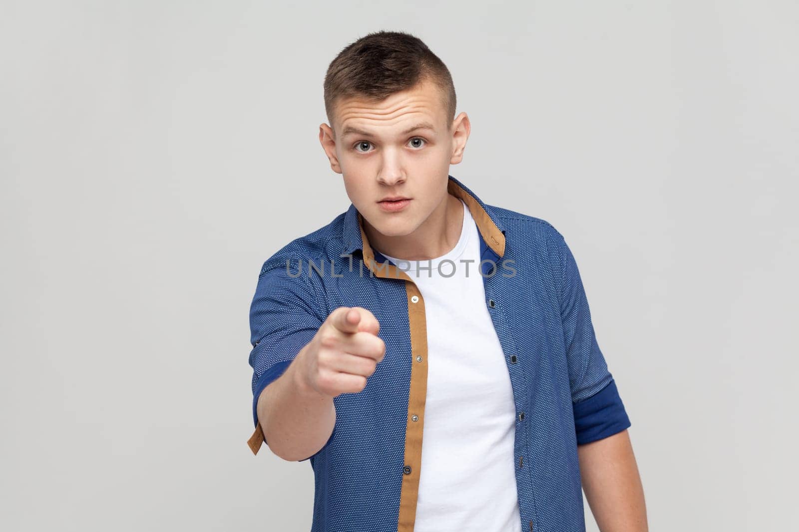 Are you ready. Portrait of handsome teenager boy wearing blue shirt pointing finger at camera choosing you, scolding and forcing to move on. Indoor studio shot isolated on gray background.