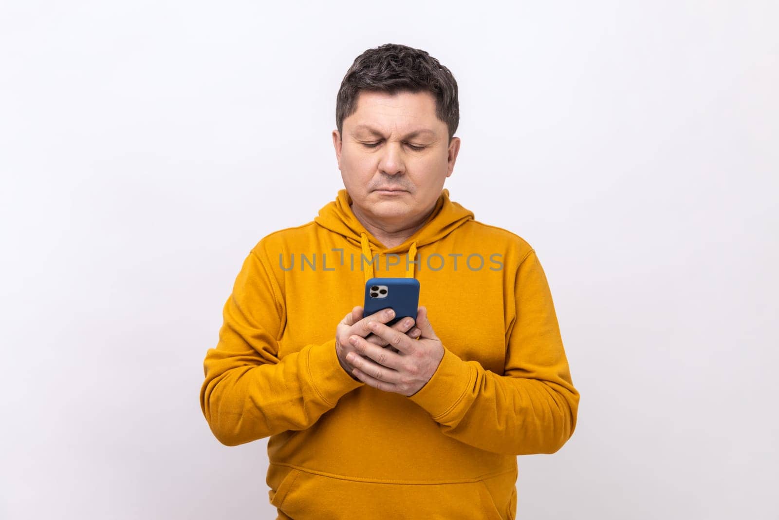 Portrait of concentrated middle aged man texting message in social media on cell phone, using mobile network services, wearing urban style hoodie. Indoor studio shot isolated on white background.
