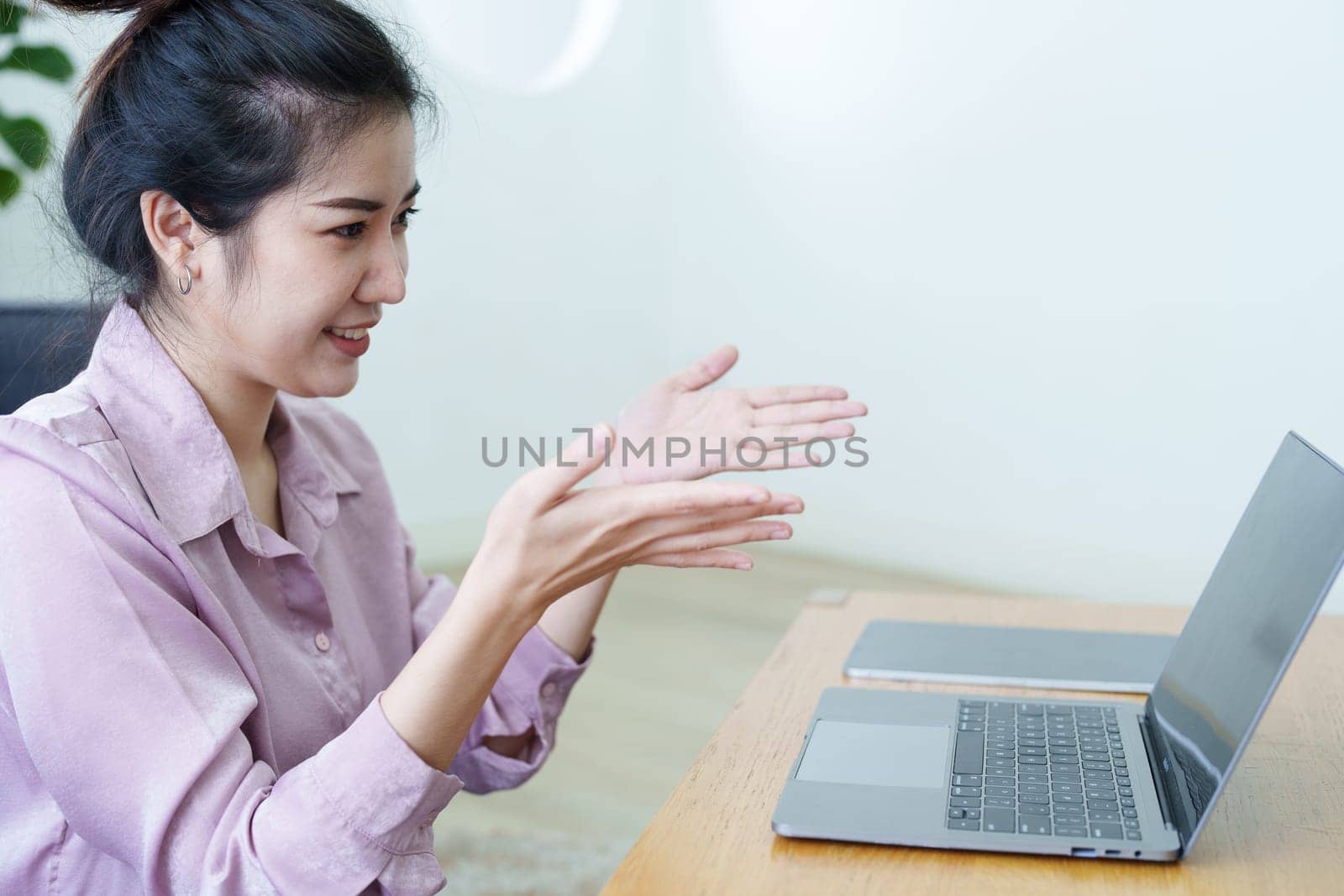 Portrait of a self-employed Asian woman using a computer doing video conference at home by Manastrong