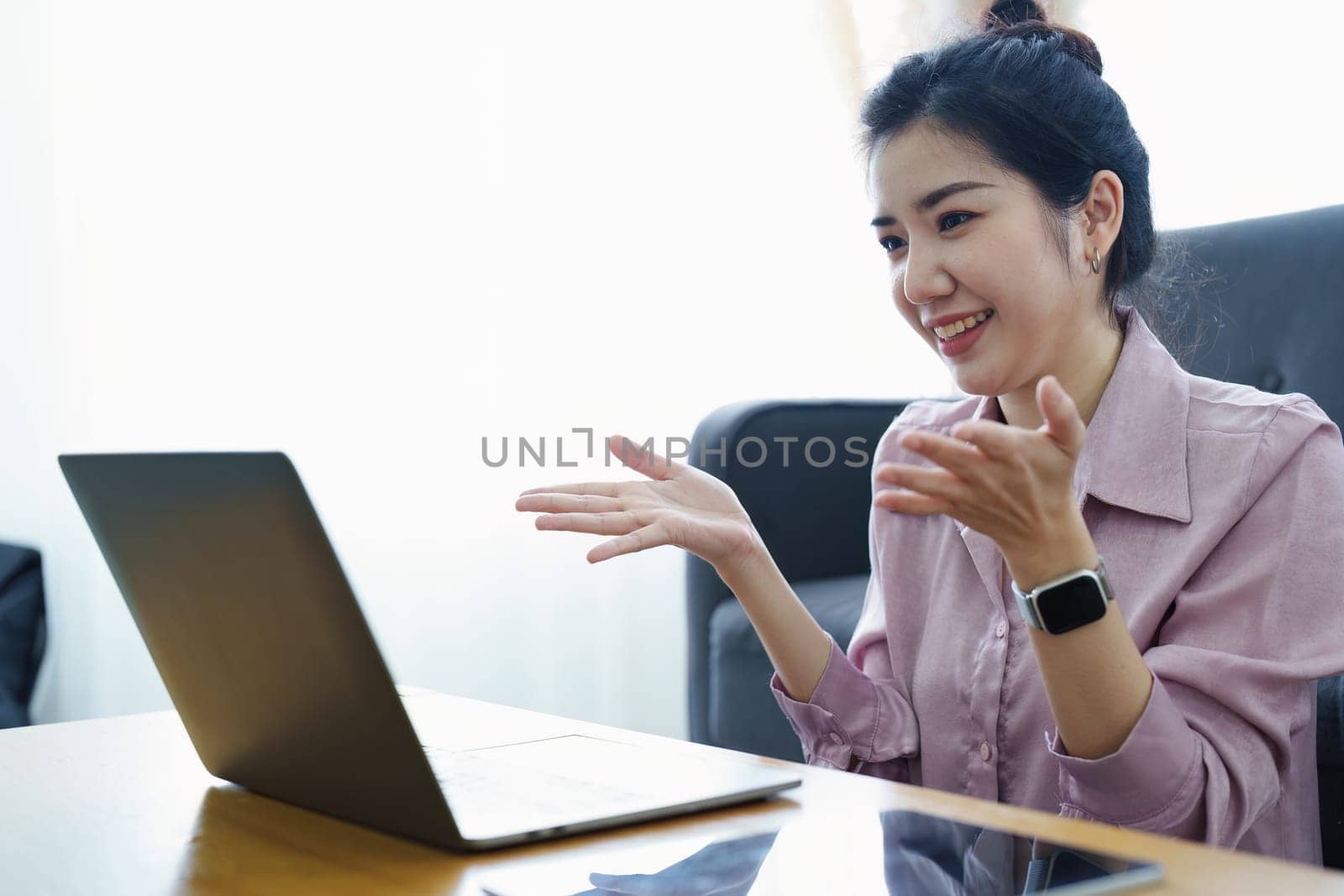 Portrait of a self-employed Asian woman using a computer doing video conference at home.