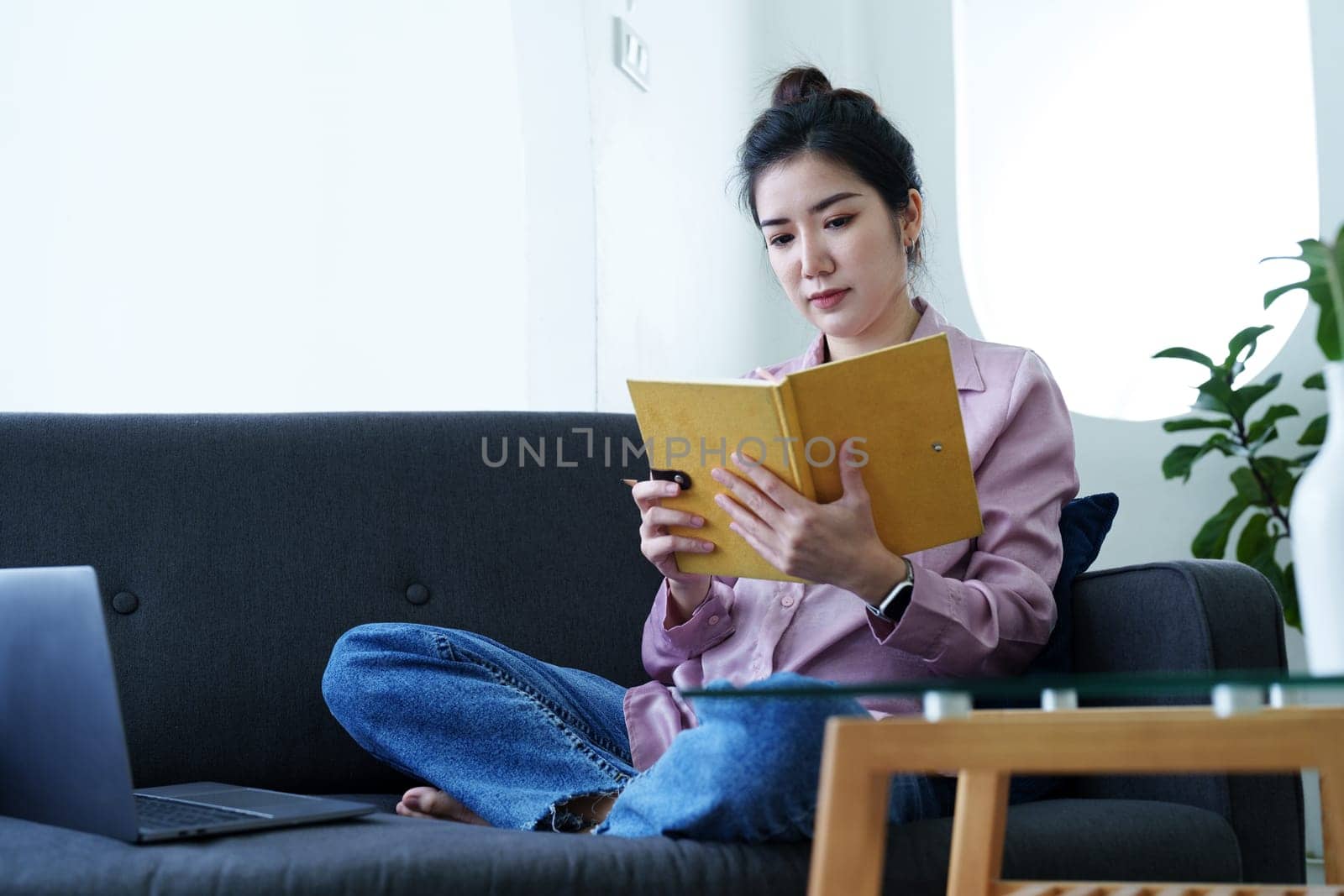 Portrait of a self-employed Asian woman holding a notebook and using a computer doing video conference at home by Manastrong