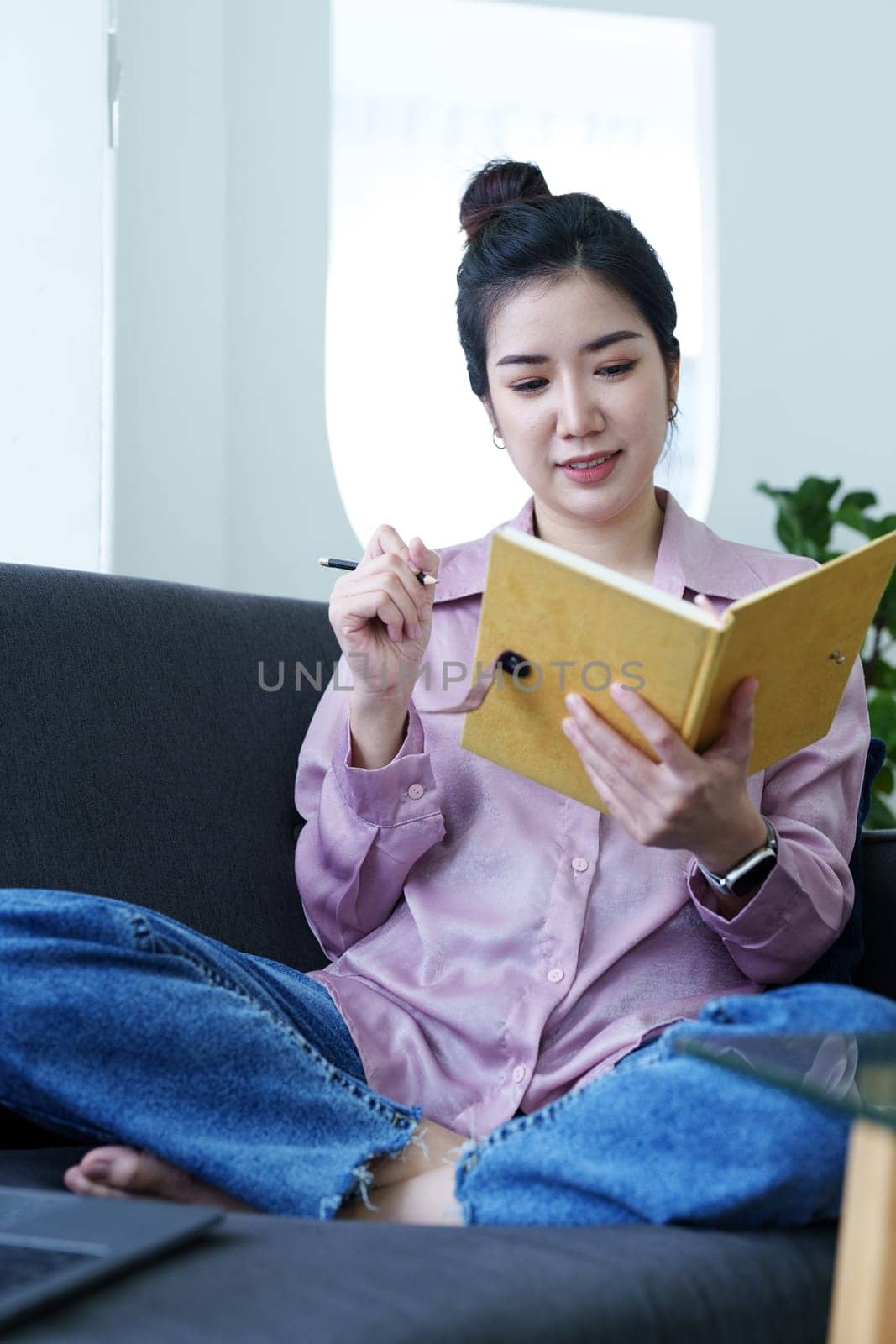 Portrait of a self-employed Asian woman holding a notebook and using a computer doing video conference at home by Manastrong