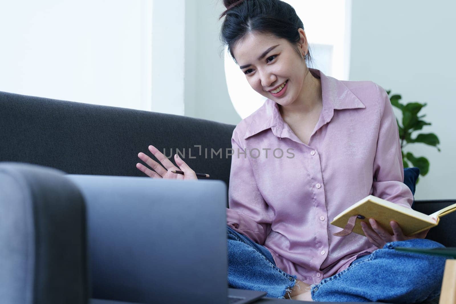 Portrait of a self-employed Asian woman holding a notebook and using a computer doing video conference at home.