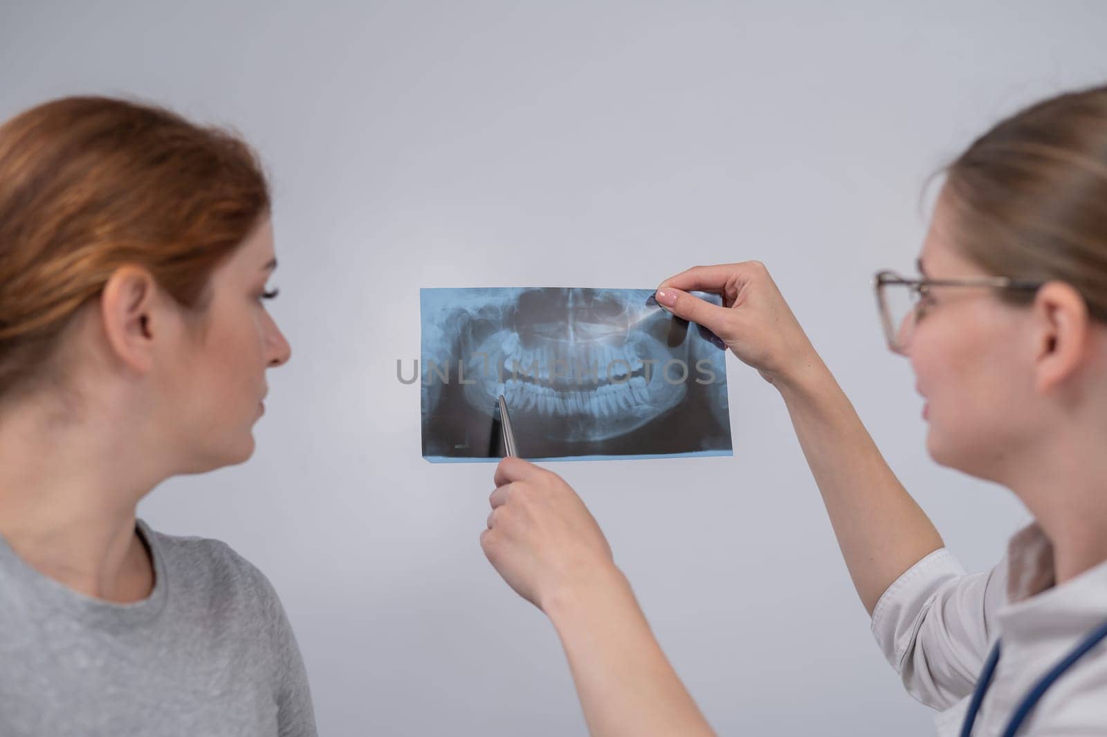 A woman doctor and a patient at the reception are discussing an x-ray of the jaw