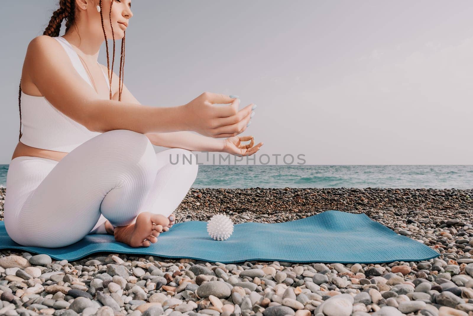 Woman yoga sea. Young woman with braids dreadlocks in white swimsuit and boho style braclets practicing outdoors on yoga mat by the ocean on sunny day. Women's yoga fitness routine. Healthy lifestyle, harmony