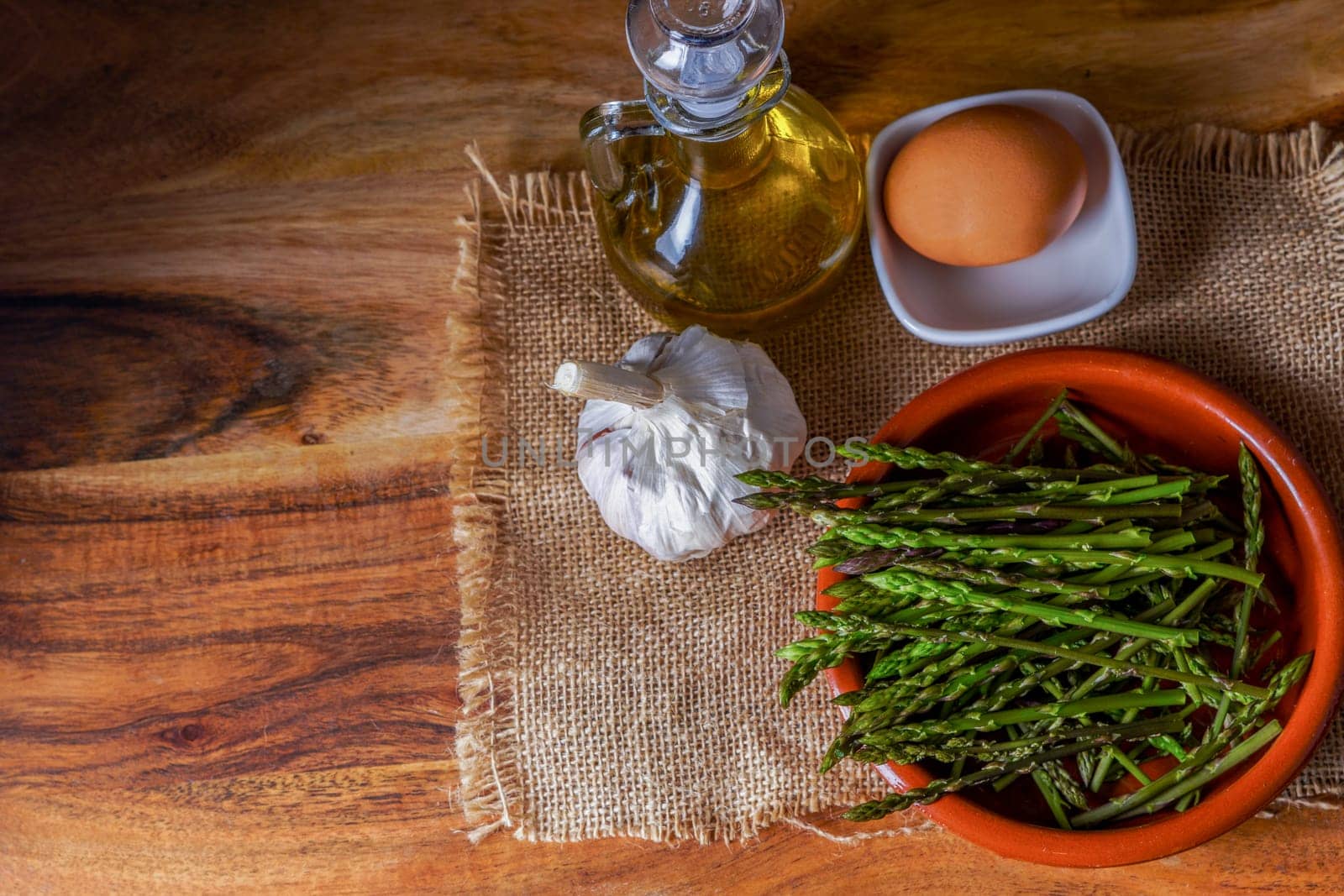 top view of wild asparagus in clay pot on a burlap cloth with eggs,olive oil and garlic