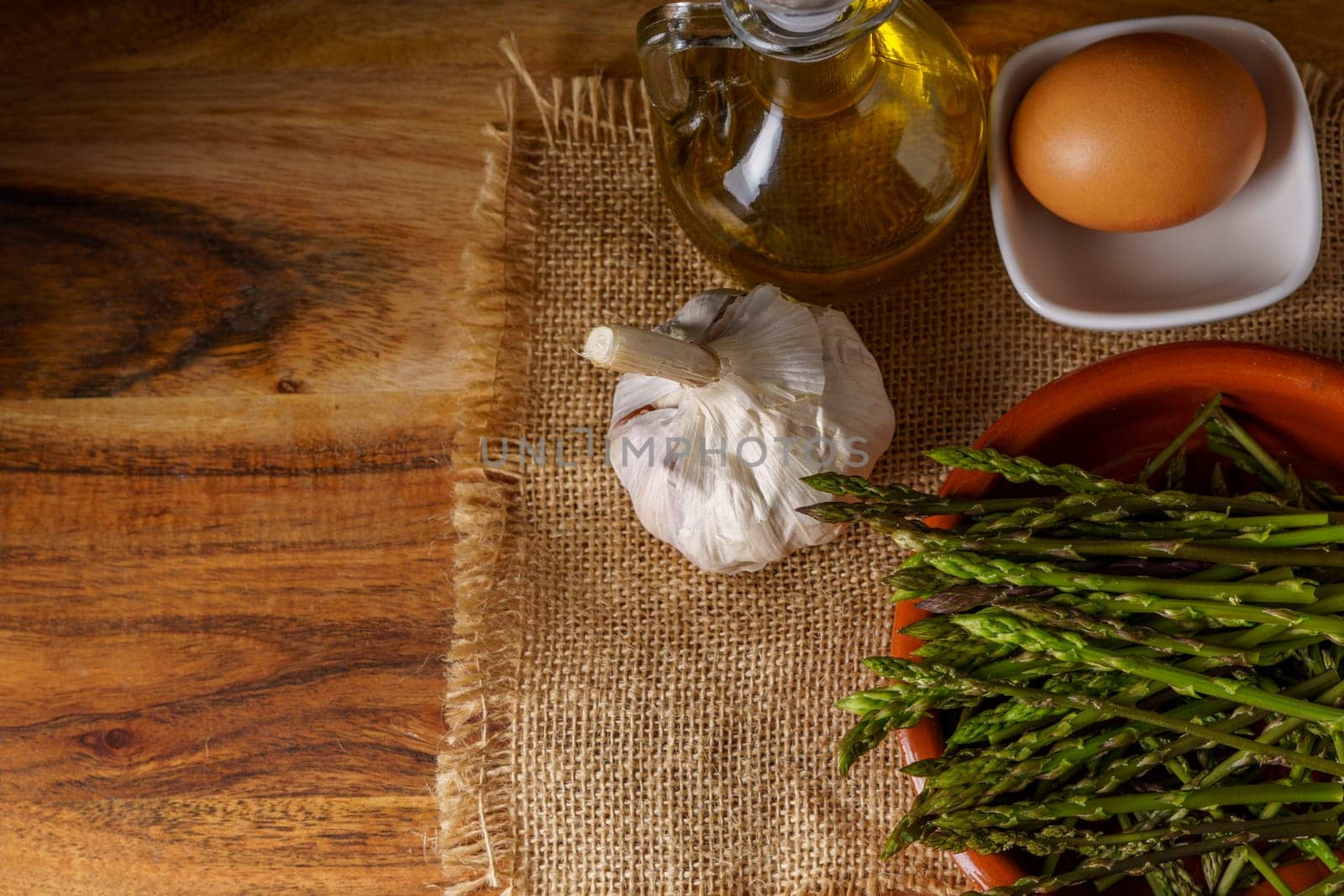 top view of wild asparagus in clay pot on a burlap cloth with eggs,olive oil and garlic
