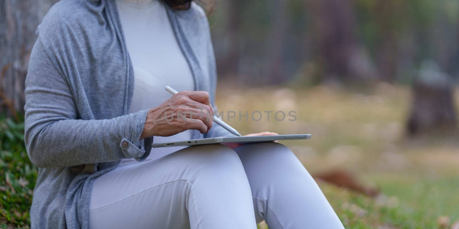Close up Cheerful overjoyed elderly woman happy and enjoying peaceful beautiful in park and drawing in digital tablet by itchaznong